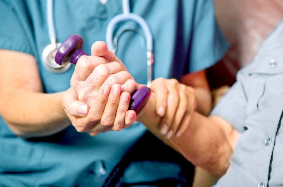 A nurse holds an older patient's hands
